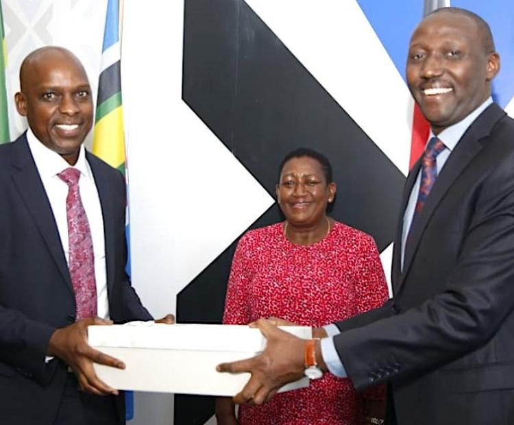 Mr. David Mugonyi (left) recieves instruments of office from his predecessor Mr. Christopher Wambua (right) when he assumed office as the Director General of the Communications Authority of Kenya today. Looking on is Ms. Mary Mungai, the CA Board Chairperson.